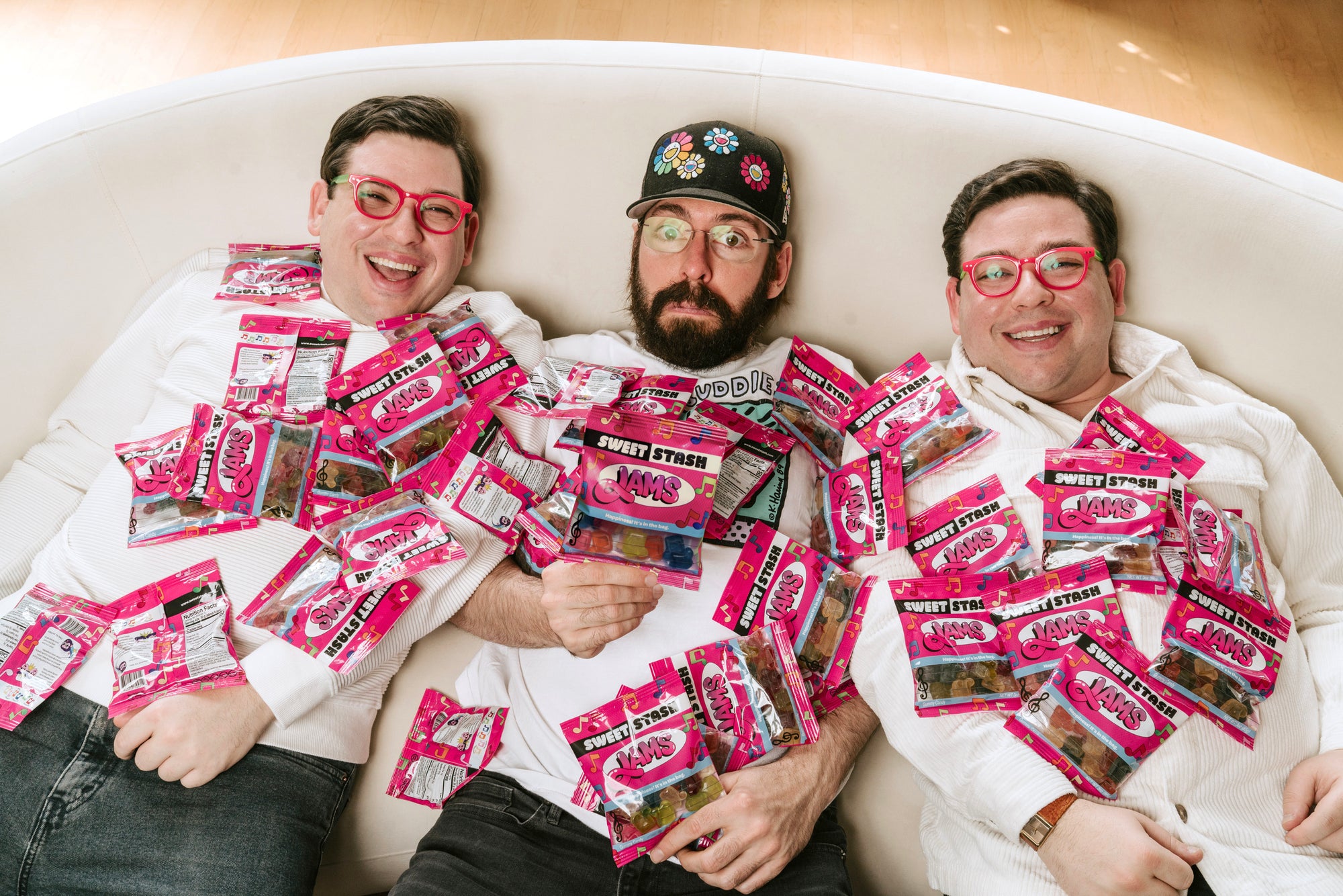 Martin Starr and the Potash Twins sitting on a couch surrounded by pink and white Sweet Stash Jams packages.